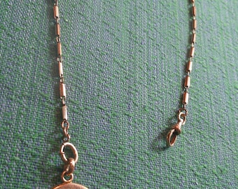 May include: A copper-toned circular locket pendant featuring an embossed floral and cross-hatched pattern, attached to a delicate metal chain with small cylindrical links and a spring-ring clasp at the end of the chain for secure fastening.
