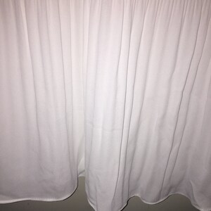 May include: White pleated fabric with a smooth texture. The fabric is gathered at the bottom, creating a ruffled edge.