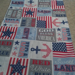 May include: A rectangular table runner featuring a patriotic patchwork print in red, white, and blue. The design includes American flags, anchors, stars, and text such as God Bless America, Sweet Land of Liberty, USA, and Red White & Blue.