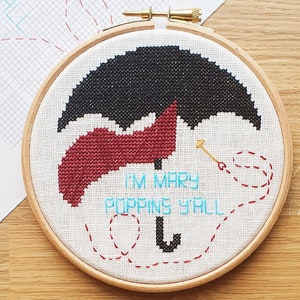 May include: A white embroidery hoop with a black and red cross-stitch design of an umbrella. The text "I'm Mary Poppins Y'all" is stitched in blue thread.
