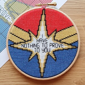 Peut inclure: Un cercle de broderie au point de croix avec un motif rouge, jaune, bleu et blanc. Le texte "I HAVE NOTHING TO PROVE TO YOU" est brodé en blanc. Le cercle est en bois.