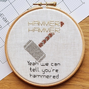 Puede incluir: Un aro de bordado blanco con un diseño de punto de cruz de un martillo y el texto "Hammer Hammer Yeah we can tell you're hammered".