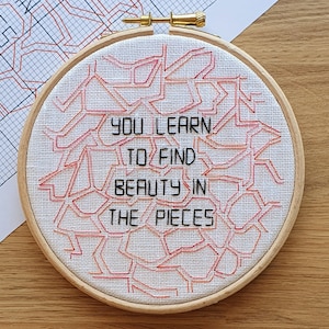 May include: White embroidery hoop with red and orange geometric patterns and the text "You learn to find beauty in the pieces".