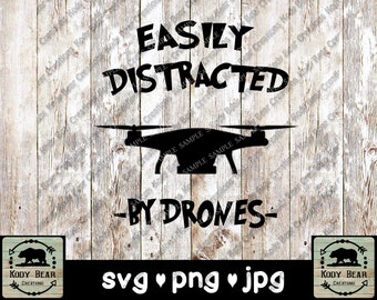May include: A black graphic design featuring the text EASILY DISTRACTED BY DRONES with a silhouette of a quadcopter drone in the center. The design is displayed over a white vertical wood plank background with repeating watermarks.
