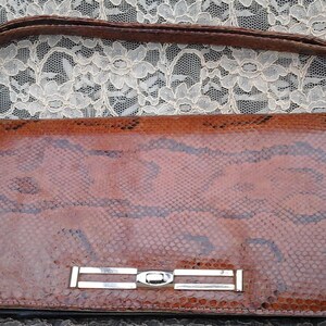 May include: A brown snakeskin clutch bag with a silver metal clasp. The bag has a strap and is made of genuine leather.