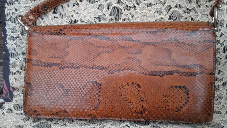 May include: A brown snakeskin shoulder bag with a silver chain strap.