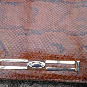 May include: A brown snakeskin clutch bag with a gold metal clasp.