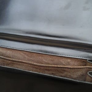 May include: A black leather clutch bag with a brown suede lining and two gold metal clasps.