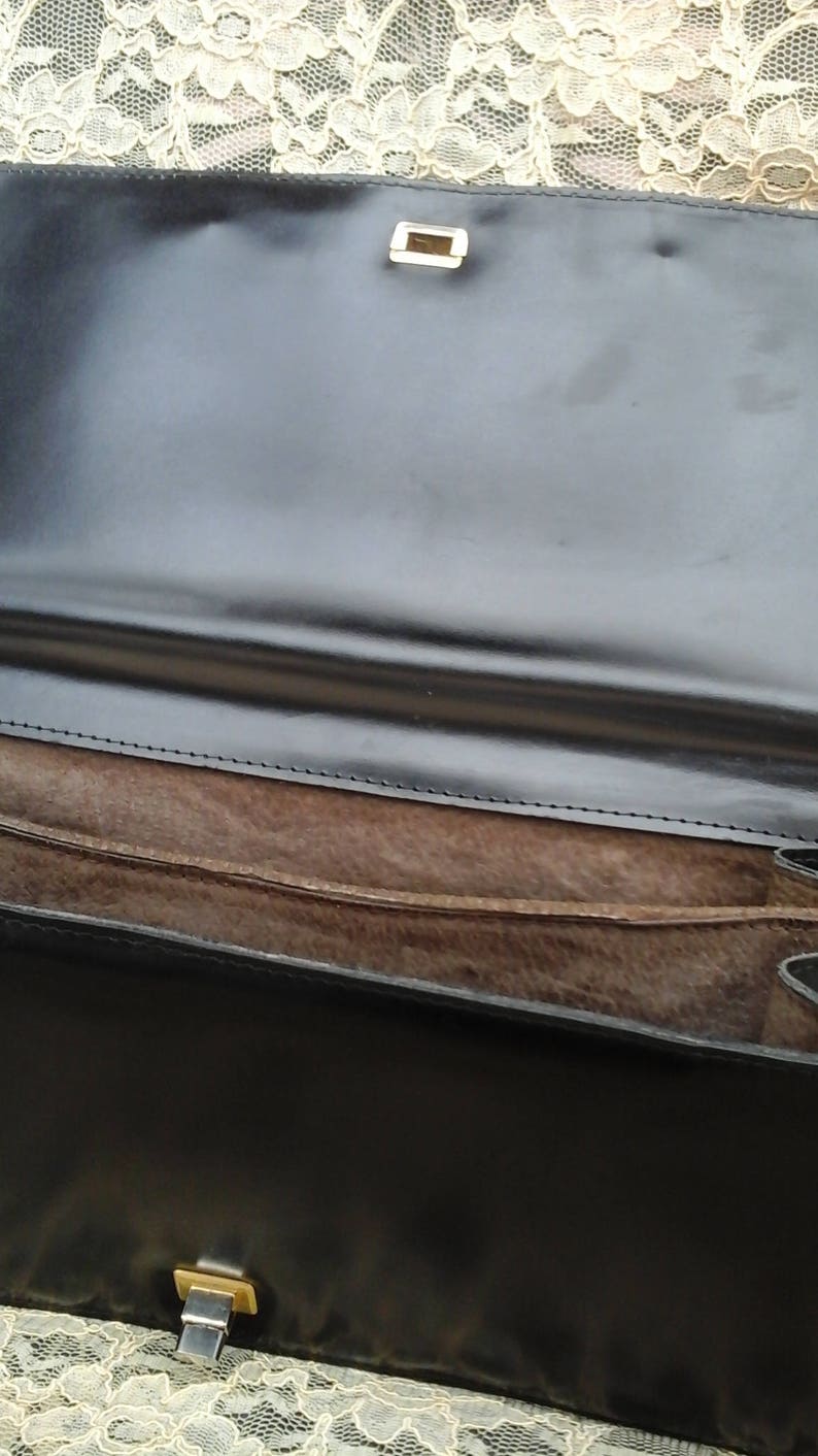 May include: A black leather clutch bag with a brown suede lining and two gold metal clasps.