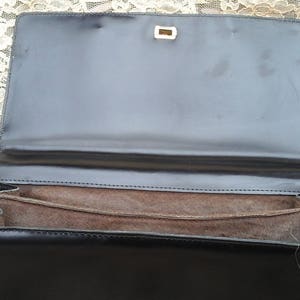 May include: A black leather handbag with a brown fabric lining and a silver clasp. The bag is open and the lining is visible.