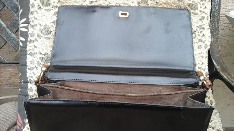 May include: A black leather handbag with a brown fabric lining and a silver clasp. The bag is open and the lining is visible.
