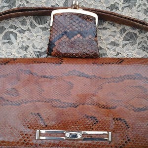 May include: A brown snakeskin handbag with a matching snakeskin purse. The handbag has a silver clasp and a strap.