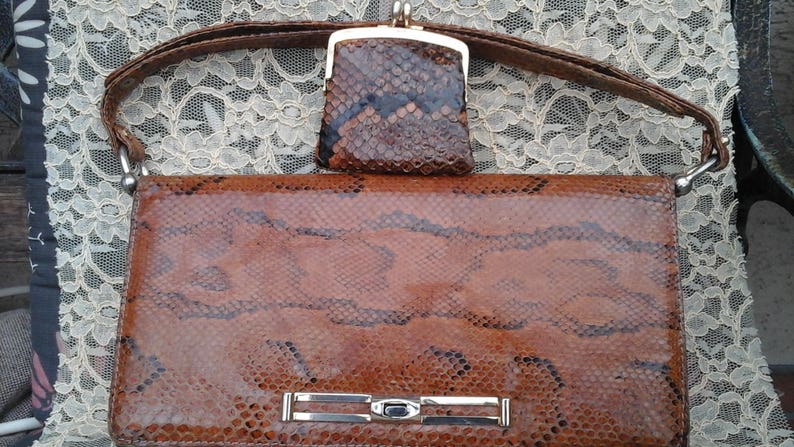 May include: A brown snakeskin handbag with a matching snakeskin purse. The handbag has a silver clasp and a strap.