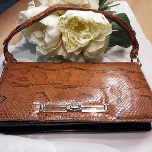 May include: A brown snakeskin clutch bag with a silver clasp and a black leather base.