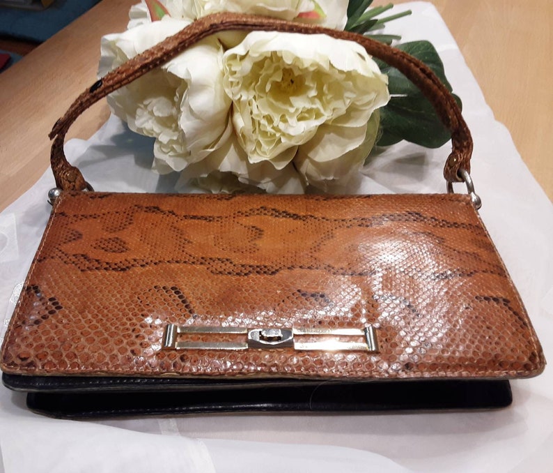 May include: A brown snakeskin clutch bag with a silver clasp and a black leather base.