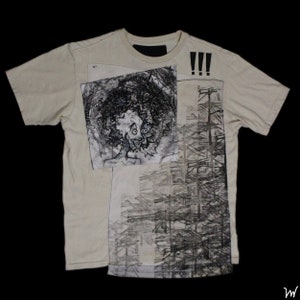 May include: A beige t-shirt with a black and white graphic print. The print features a stylized face with large eyes and a geometric pattern. The text "!!!" is printed on the right side of the shirt.