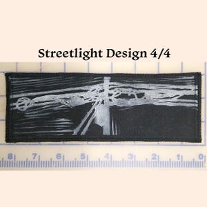 May include: A black and white linocut print of a streetlight on a black fabric background. The print is titled "Streetlight Design 4/4".