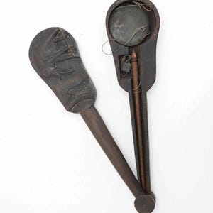 May include: Two antique wooden scales with dark brown handles and carved details. One scale features a carved design of a building and figures. The other scale has a circular metal plate and string. The scales are set against a white background.