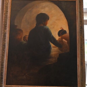 May include: An oil painting in a gold ornate frame depicts three figures in a dimly lit interior. The central figure, seen from the back, wears a dark green garment. The painting has a warm, earthy color palette, with a focus on light and shadow.