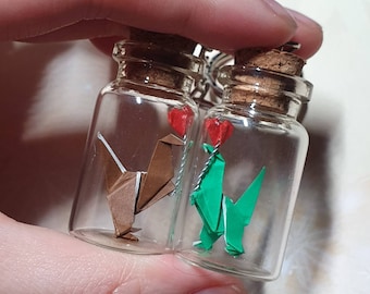 Pair of miniature origami dinosaurs holding origami hearts in glass vials