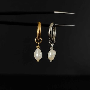 May include: Two hoop earrings with a pearl drop. The hoop on the left is gold and the hoop on the right is silver.