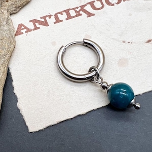 Puede incluir: Un aro de plata para la oreja con un colgante de piedra turquesa. El arete está sobre un fondo blanco con la palabra "ANTIKUOS" impresa en él.