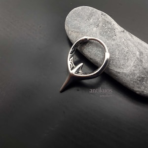 Puede incluir: Pendiente de aro de plata con un dise&ntilde;o puntiagudo detallado. El pendiente est&aacute; sobre un fondo de piedra gris. El texto "antikuos jewellery" es visible debajo del pendiente.