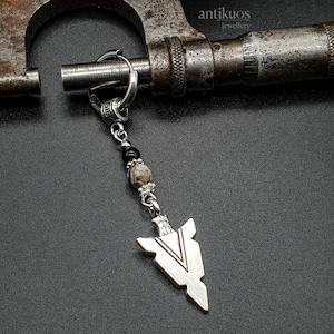 May include: A silver arrowhead keychain with a black and white stone bead. The keychain is hanging from a silver ring.