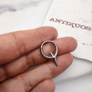 Puede incluir: Un aro de plata para la oreja con un dise&ntilde;o puntiagudo. El aro es de metal y tiene una superficie texturizada.