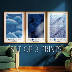 Op de afbeelding: Set van drie ingelijste kunstdrukken met abstracte blauwe ontwerpen. Elke print zit in een houten lijst en bevat de tekst "YAYOI KUSAMA" en Japanse tekst. De prints worden weergegeven op een donkerblauwe muur met een groene bank.