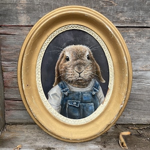 May include: A painting of a brown rabbit wearing a blue denim overall and a white shirt. The rabbit is framed in a gold oval frame.