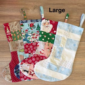 May include: Four large Christmas stockings with patchwork designs. The stockings feature festive patterns including Santa Claus, snowflakes, and gingerbread men. Each stocking has a loop for hanging and is made of fabric in red, blue, green, and white.