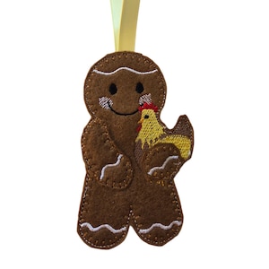 May include: A brown felt gingerbread man decoration holding a yellow and brown chicken. The ornament has white stitching and a yellow ribbon for hanging. A festive Christmas decoration.