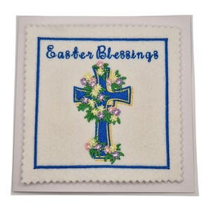 May include: An Easter card featuring a blue cross embroidered with flowers. The card has a white background, a blue border, and the words "Easter Blessings" in blue script.