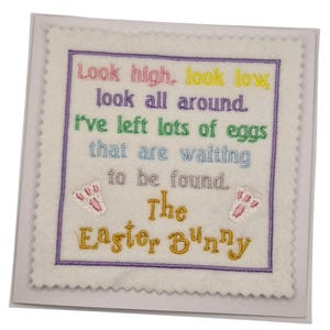 May include: A square, off-white Easter-themed felt decoration with embroidered text and accents. The text reads "Look high, look low, look all around. I've left lots of eggs that are waiting to be found. The Easter Bunny."