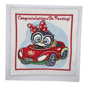 May include: Embroidered card with a red border and the text "Congratulations On Passing!". The card features a cartoon penguin wearing a bow and driving a red car with a rainbow on the side. The background is light blue.
