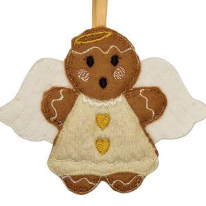 Könnte beinhalten: Ein Weihnachtsornament in Form eines Lebkuchenengels aus Filz. Das Ornament hat einen braunen Lebkuchenkörper mit weißen Flügeln und einem cremefarbenen Kleid. Der Engel hat einen goldenen Heiligenschein und zwei gelbe Herzakzente auf dem Kleid. Ein goldenes Band zum Aufhängen ist befestigt.