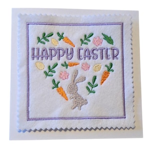 May include: A white square Easter card with a purple embroidered border and a heart-shaped design. The design includes the text "HAPPY EASTER", a gray bunny, orange carrots, green leaves, pink flowers, and yellow eggs.