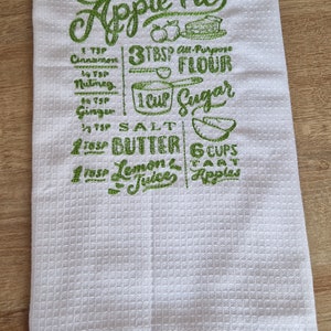 Könnte beinhalten: Weißes Küchenhandtuch mit Waffelstruktur und grün gesticktem Text und Illustrationen. Der Text lautet "Homemade Apple Pie" mit einem Rezept, das Zutaten wie Mehl, Zucker und Äpfel enthält. Eine charmante Ergänzung für jede Küche.