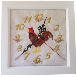 May include: Square white framed wall clock with an embroidered rooster design. The clock face is white with gold numerals and a brown rooster in the center. The clock hands are black, and the second hand is red.