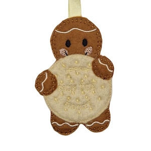 May include: A brown felt gingerbread man decoration holding a cream-coloured cookie. The cookie has gold embroidered text and gold dot accents. The gingerbread man has black eyes, stitched details, and a yellow ribbon for hanging.