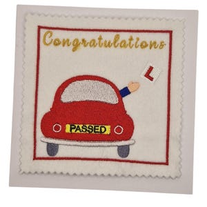 May include: A white card with a red border features a red car with the word "PASSED" on the license plate. The card has the word "Congratulations" in gold script above the car. A hand holding an "L" sign is visible.