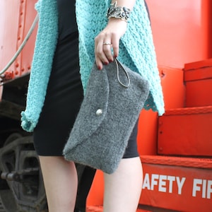 May include: A woman wearing a teal crochet cardigan and a black dress, standing in front of a red train car. She is holding a gray clutch purse and wearing black heels. The train car has the words "Safety First" printed on the side.