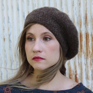 May include: A brown beret made of a soft, fuzzy material. The beret is worn on the head of a person with long, brown hair.