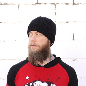 May include: A person wearing a black knitted beanie and a red and black baseball jersey with a white star and a graphic print.