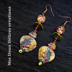 Puede incluir: Pendientes artesanales con diseño de loro. Los pendientes tienen ganchos de cobre, un loro amarillo, verde y morado, y un diseño floral. También tienen una cuenta amarilla en la parte inferior y una cuenta floral en la parte superior.