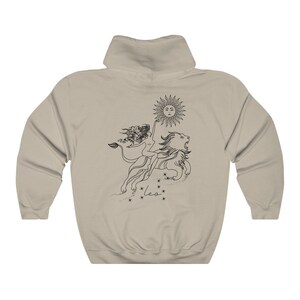 May include: A tan hoodie with a black and white illustration of a woman riding a lion with a sun above them. The text "Leo" is below the illustration.