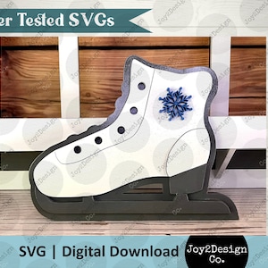 May include: White ice skate with a blue snowflake design. The skate is on a wooden surface. SVG | Digital Download Joy2Design Co.