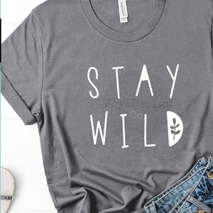 May include: A gray t-shirt with the text "STAY WILD" in white lettering. A small white leaf design is next to the word "WILD".