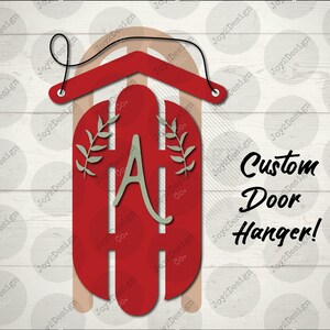 May include: Red wooden door hanger with a white letter A and green leaves. The hanger is shaped like a house and has a rope loop for hanging. The text "Custom Door Hanger!" is written in black on a white background.